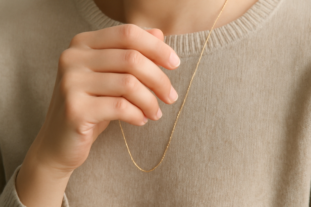 main portant un collier fin sur pull uni
